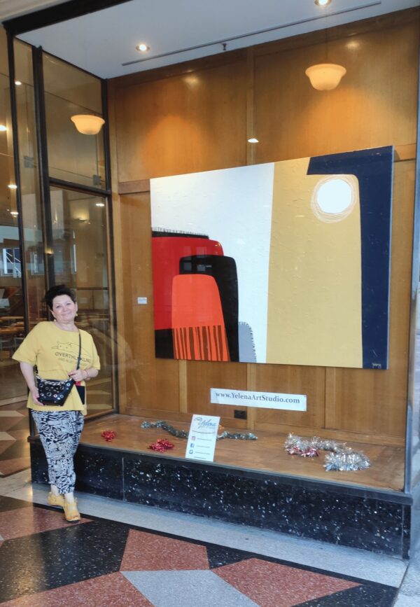 Yelena Revis standing beside her abstract painting Silent Expanse in a gallery exhibition window